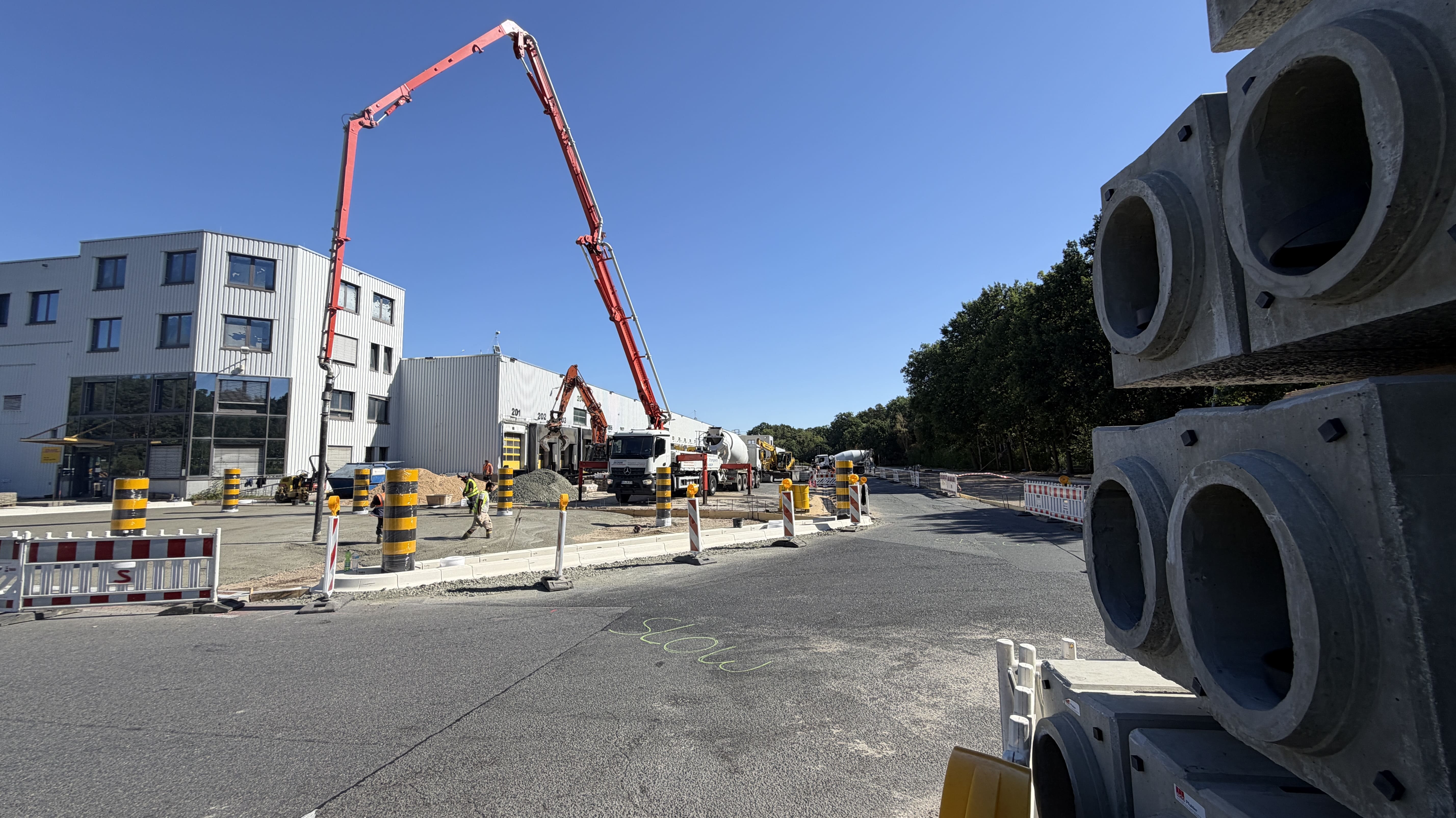 Betonpumpe im Einsatz auf dem Gelände des Logistikzentrums mit Betonrohren im Vordergrund.
